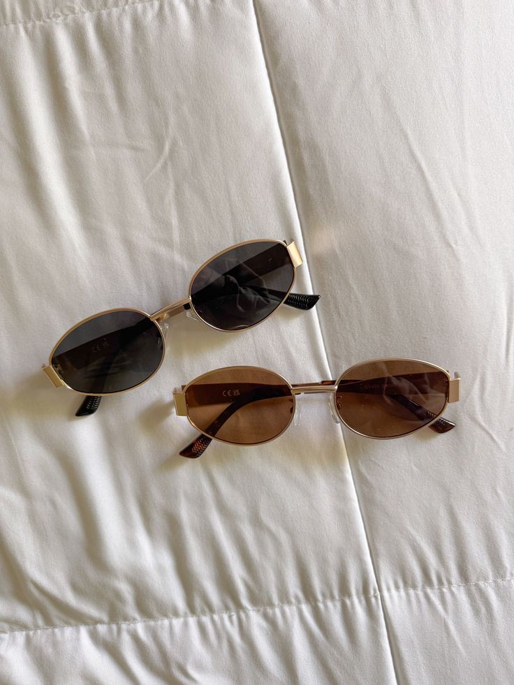 summer sunglasses outfitidea summerstyle - Handy Home Two pairs of stylish oval sunglasses with gold frames on a white quilted surface, perfect for sunny days and fashion statements.