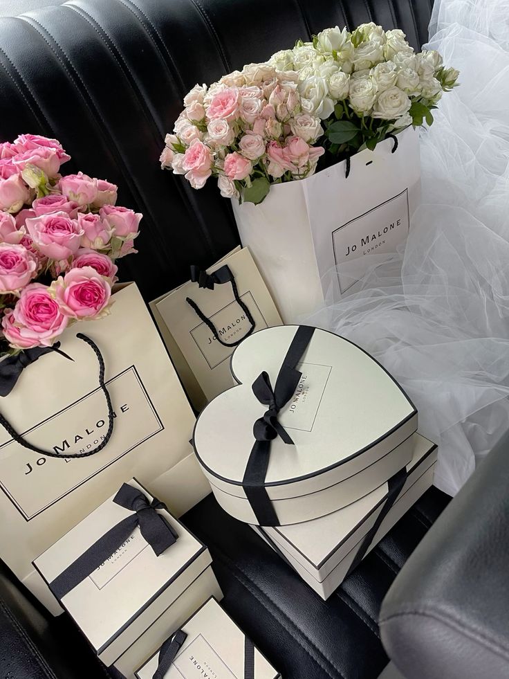 Elegant Jo Malone gift bags and heart-shaped boxes adorned with pink and white roses on a leather seat.