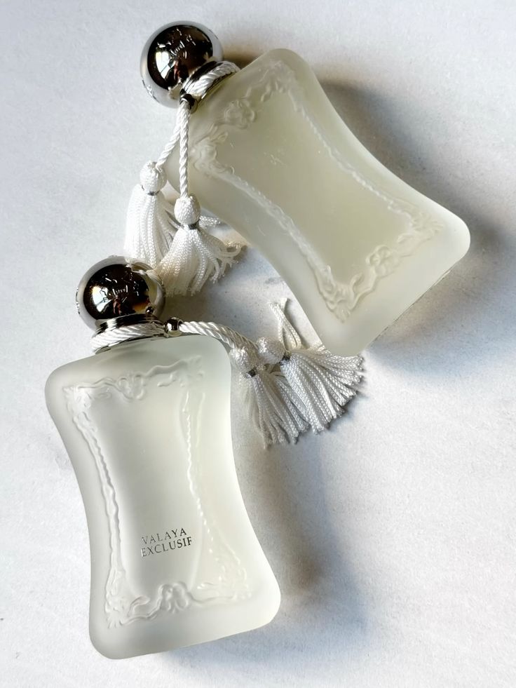 Elegant frosted perfume bottles with silver caps and tassels, labeled Valaya Exclusif, on a light background.