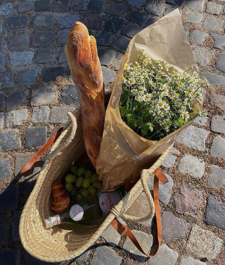 02b1756a-9fe7-4df8-879c-fe7197dde090 - Handy Home Wicker basket with baguette, bouquet, grapes, and water on cobblestone street, perfect for a sunny picnic day.