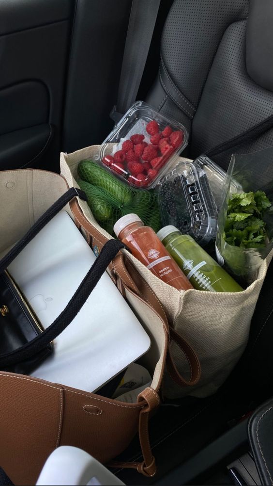 Reusable tote bag on car seat with fresh raspberries, cucumbers, juices, and laptop. Eco-friendly shopping and commuting essentials.