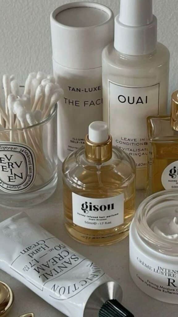 Assorted skincare and hair products including lotions and perfumes, neatly arranged with cotton swabs in a glass holder.