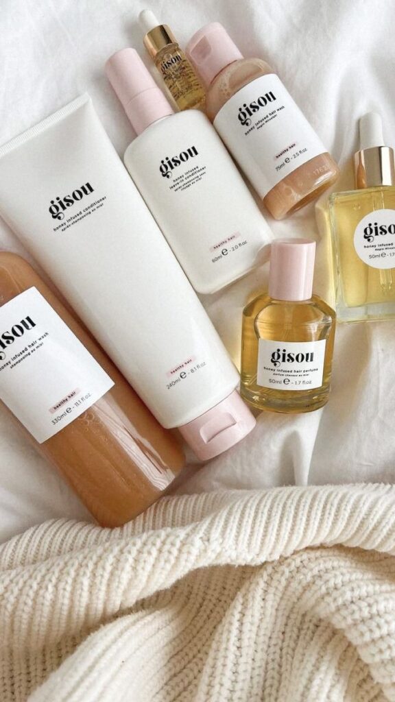 Gisou hair care products on a cozy white blanket, including honey-infused shampoo, conditioner, and hair oil.