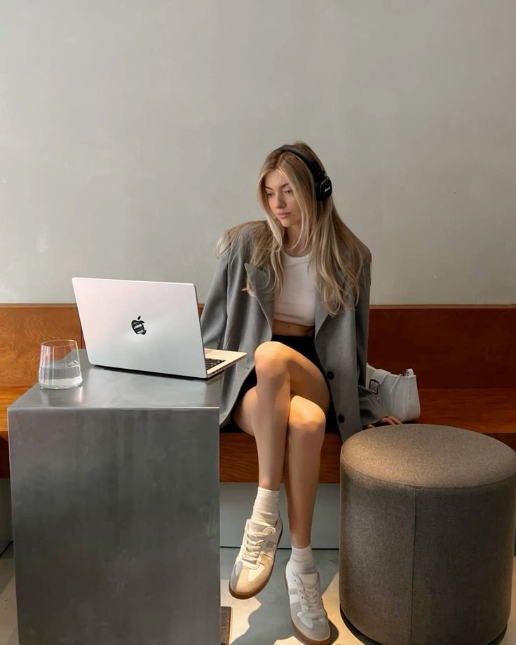 Young woman with headphones working on a laptop in a stylish cafe, wearing casual attire and sneakers, seated at a modern bench.