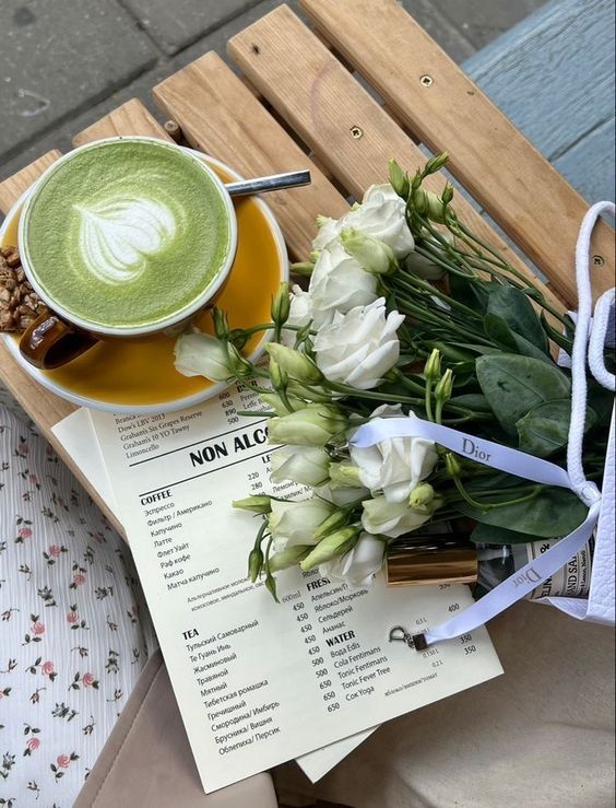 Cup of matcha latte on a wooden table with white flowers and a menu, creating a cozy cafe vibe.