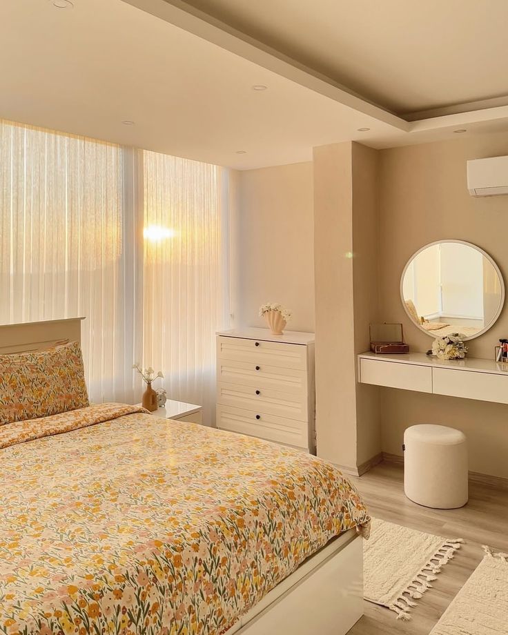 Cozy bedroom with floral bedding, white furniture, and round mirror reflecting warm sunrise through sheer curtains. Peaceful and inviting space.