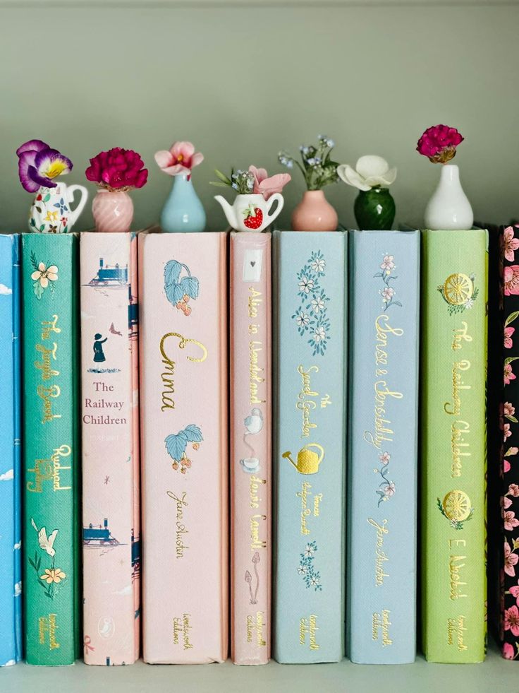 Colorful classic books with floral decorations on a shelf. Miniature vases with flowers adorn the tops. Vintage and elegant display.
