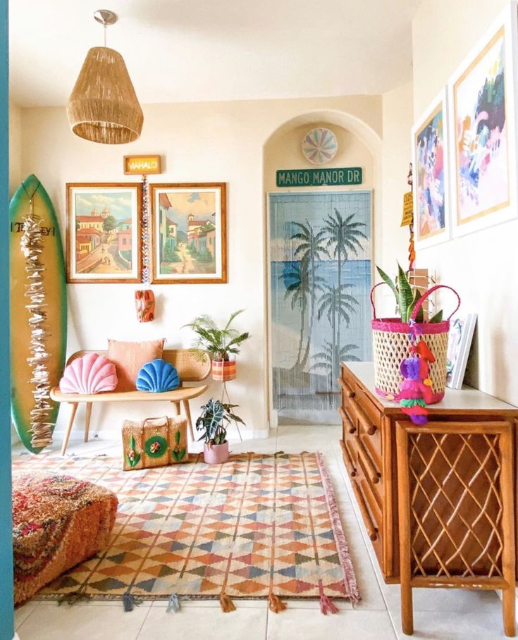Colorful boho living room with beach-themed decor, surfboard, wicker furniture, palm wall art, and vibrant rug. Cozy tropical vibe.