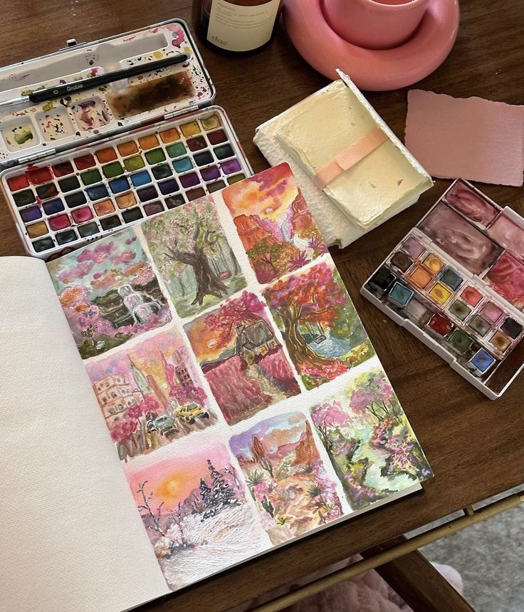 Watercolor painting set and sketchbook with vibrant landscape art pieces on a wooden table.