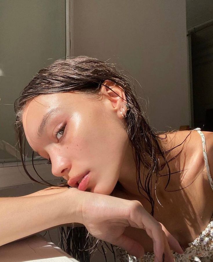 Woman with wet hair gazing towards the camera in sunlight, showcasing natural beauty and fresh skin in a serene setting.