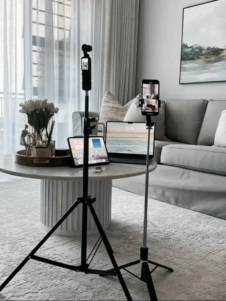 Modern living room with tech setup: tripods, tablets, and phone for productivity or content creation on a coffee table.