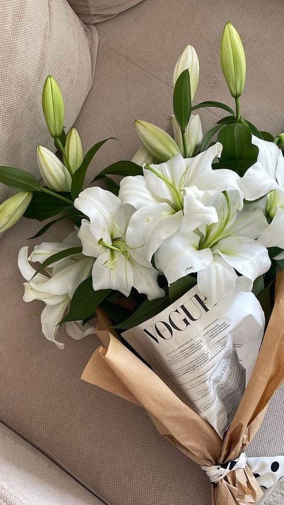 Bouquet of white lilies and a Vogue magazine wrapped in brown paper on a beige couch.