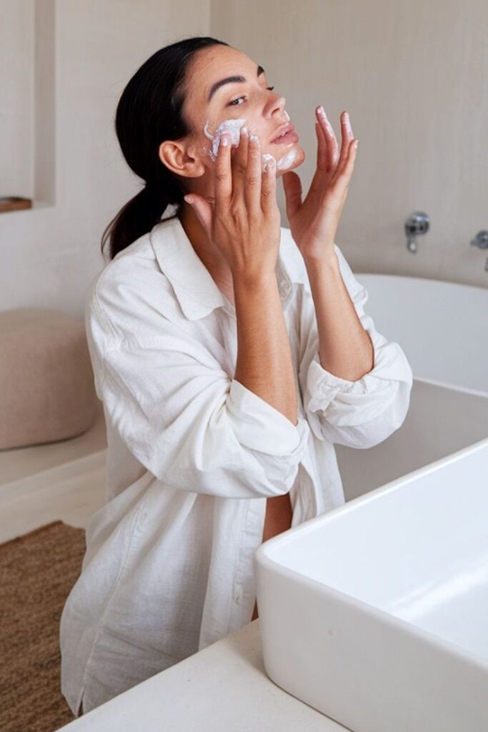 Woman applying facial cream in bright bathroom, enhancing skincare routine for radiant, healthy complexion.