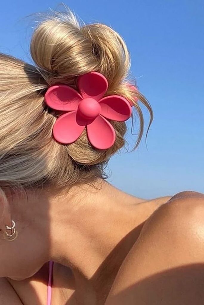 Blonde hair in a bun with pink flower clip against blue sky; summer hair accessory inspiration.