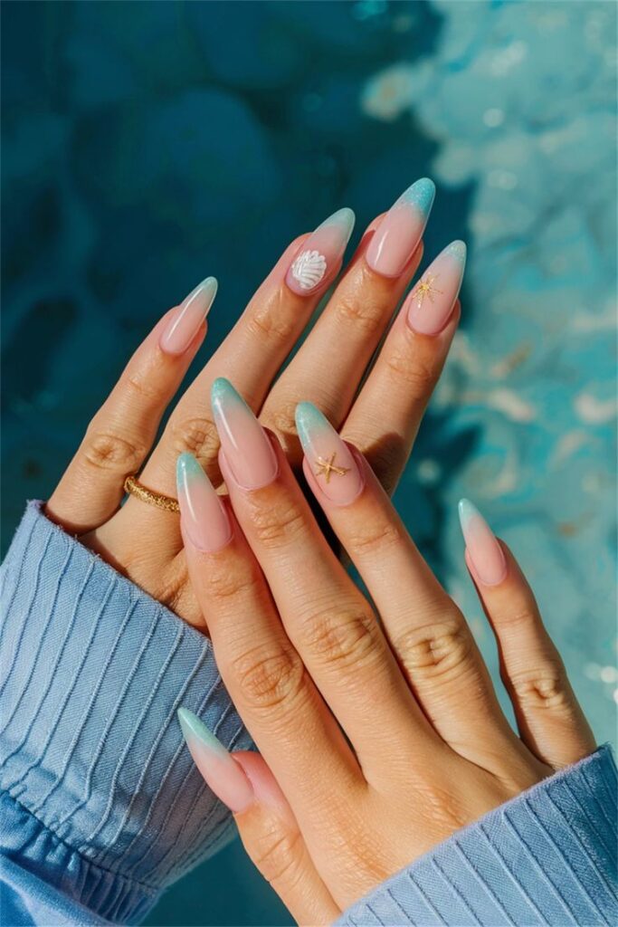 Stylish blue ombre manicure with shell and starfish designs on long nails, hand model wearing a blue sweater.