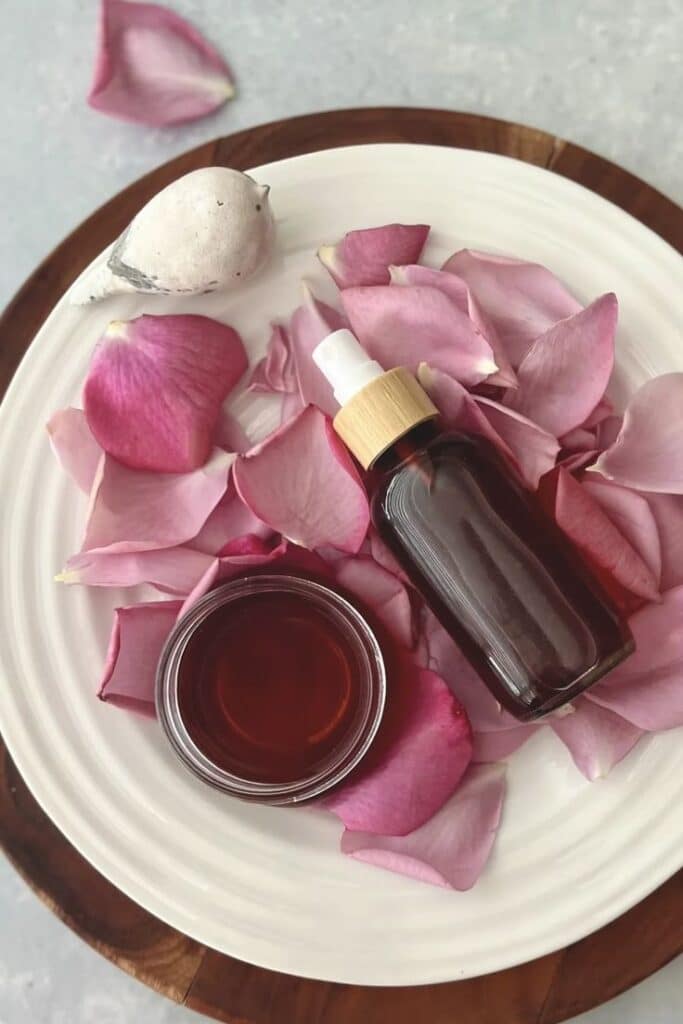 Rose petal skincare: glass bottle and bowl on petals, bird figurine on plate. Natural beauty concept.