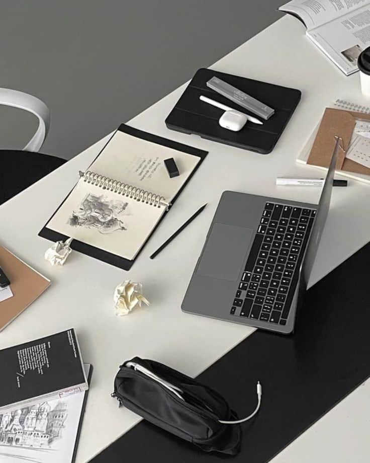 Organized workspace with laptop, notebooks, and art supplies on a black and white desk. Perfect for productivity and creativity.