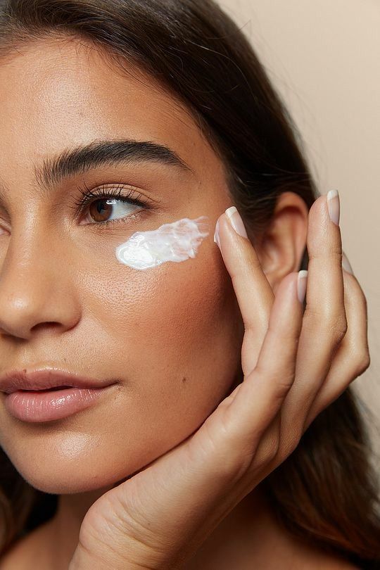 Woman applying moisturizer under eye for skincare routine.