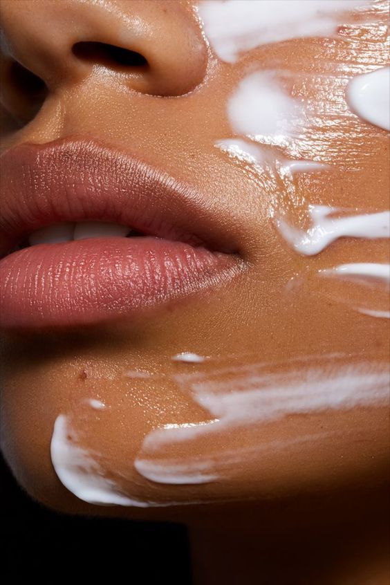 Close-up of a woman's face with smooth skin, applying white cream for skincare routine, highlighting lips and creamy texture.