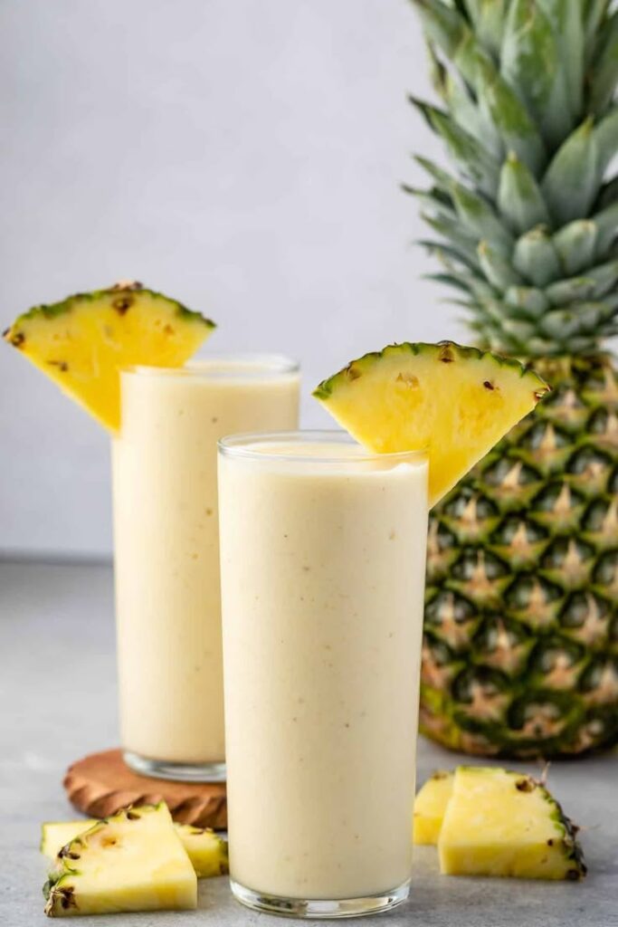 Refreshing pineapple smoothie in tall glasses with fresh pineapple garnish, perfect for a tropical treat or healthy breakfast.