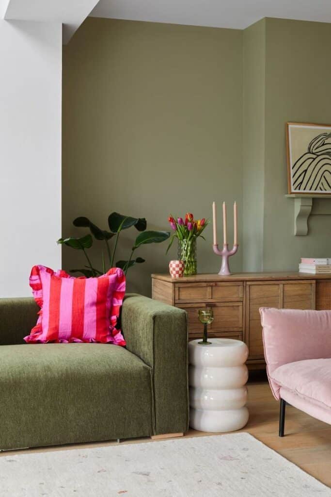 Stylish living room with green sofa, pink cushion, wooden cabinet, and modern decor. Cozy, colorful interior design.