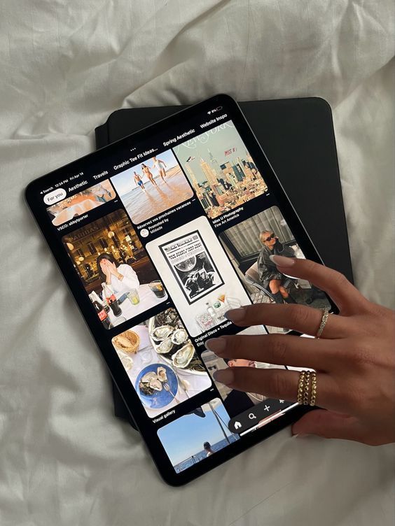 Person browsing Pinterest on a tablet, exploring travel and lifestyle inspirations, wearing gold rings.