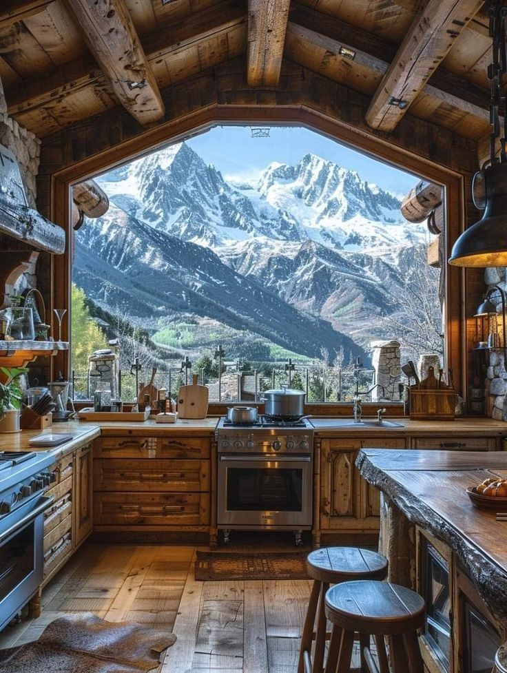 Cozy rustic kitchen with a breathtaking mountain view through a large window, featuring wooden countertops and modern appliances.