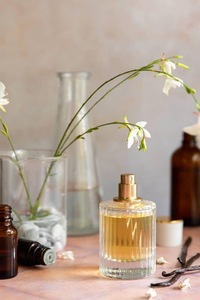 Elegant perfume bottle with floral decor on table, surrounded by flowers and amber glass bottles in a serene setting.