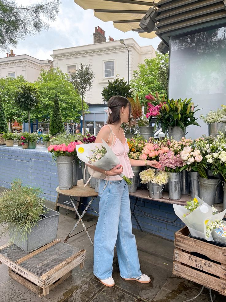 Woman selecting flowers at an outdoor market stall, surrounded by colorful bouquets on a sunny day.