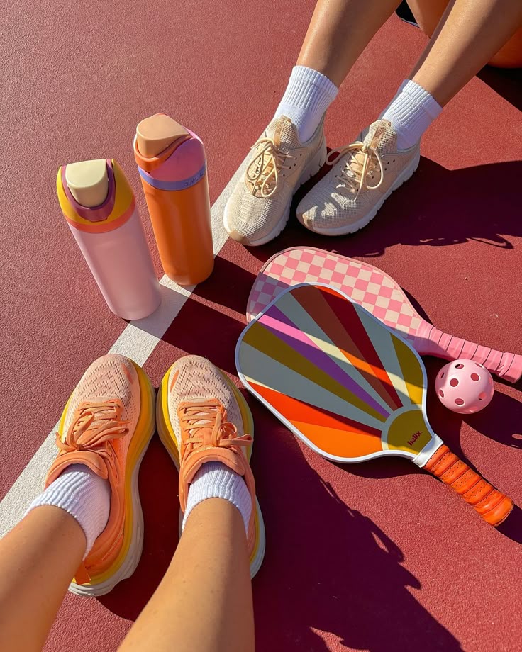 Colorful pickleball paddles, orange sneakers, and water bottles on a sunny court, ready for a vibrant game.