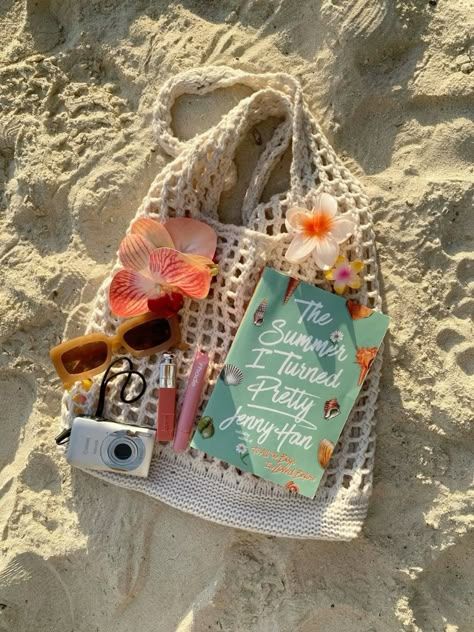 Beach essentials: woven bag, book, sunglasses, flowers, and camera on sand. Summer vibes and relaxation.
