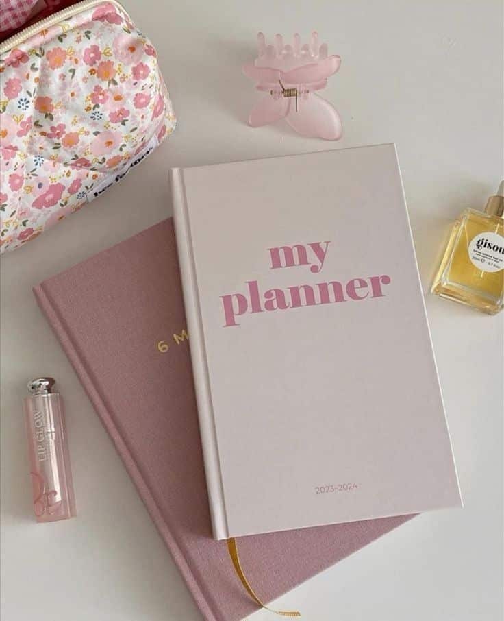 Stylish 2023-2024 planner on desk with hair clip, floral pouch, and perfume, ideal for organizing and planning your year.