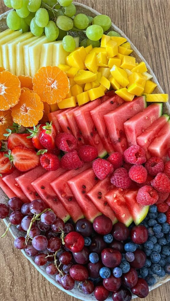 A vibrant platter of assorted fresh fruits including watermelon, grapes, mango, blueberries, and citrus on a wooden table.