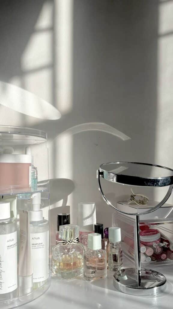 Elegant vanity setup with skincare bottles, perfumes, and a mirror, bathed in soft sunlight against a neutral background.