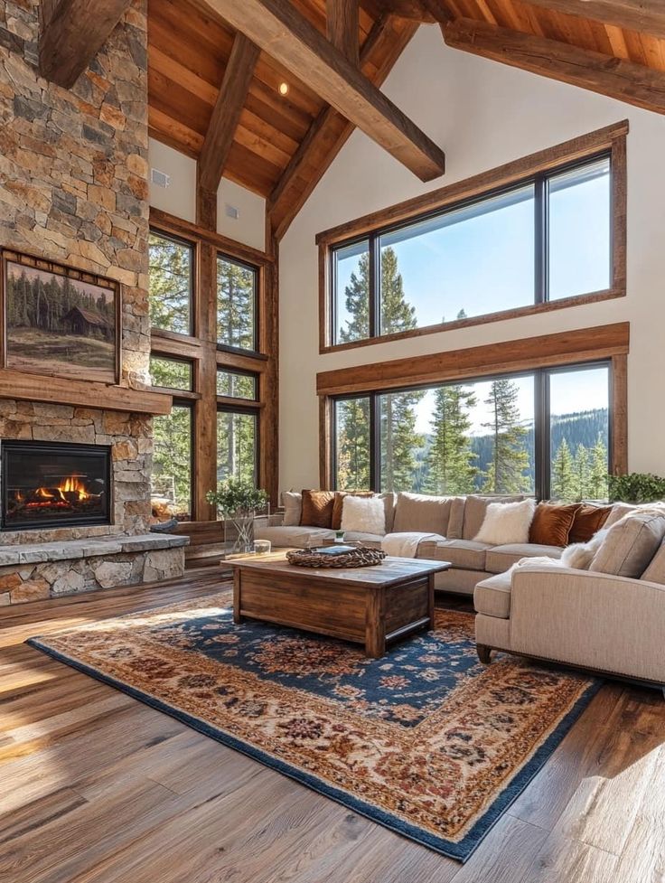 Cozy rustic living room with stone fireplace, large windows, wooden beams, and a plush beige sectional sofa. Perfect cabin retreat.