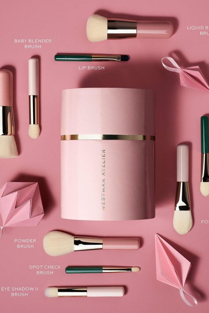 Elegant pink makeup brush set by Westman Atelier on a pink background, featuring various brushes like powder and lip brush.