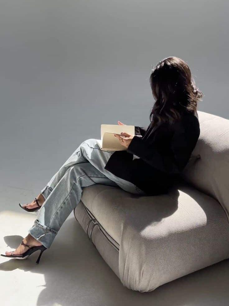 Woman seated on a modern chair, reading a book in a minimalist setting with natural light.