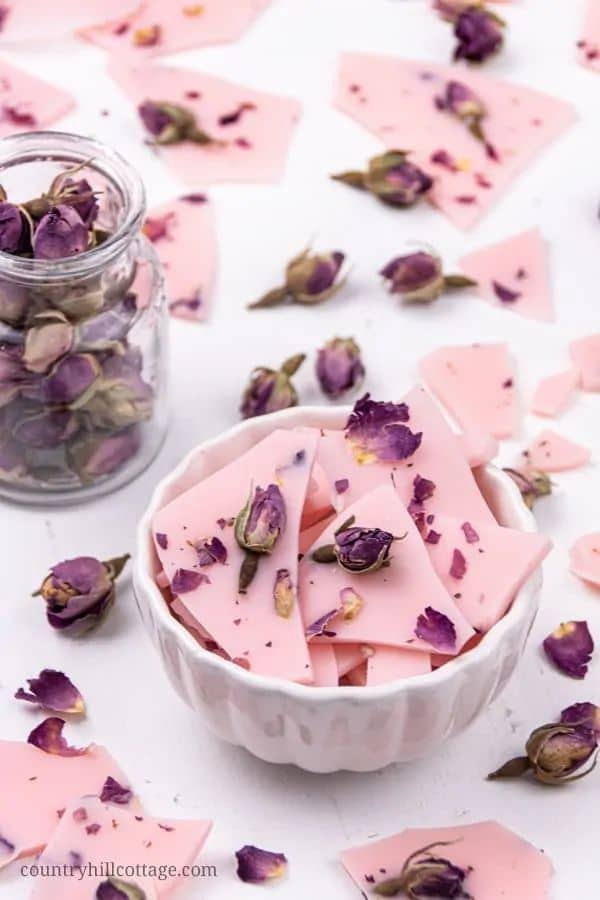 Pink chocolate bark with dried rose petals in a bowl, surrounded by dried roses and chocolate pieces. Elegant and floral dessert.