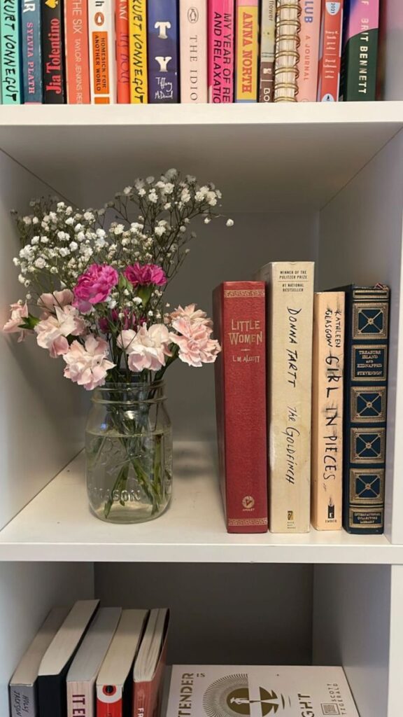 Bookshelf with novels and a jar of flowers; aesthetic reading nook and literary inspiration.