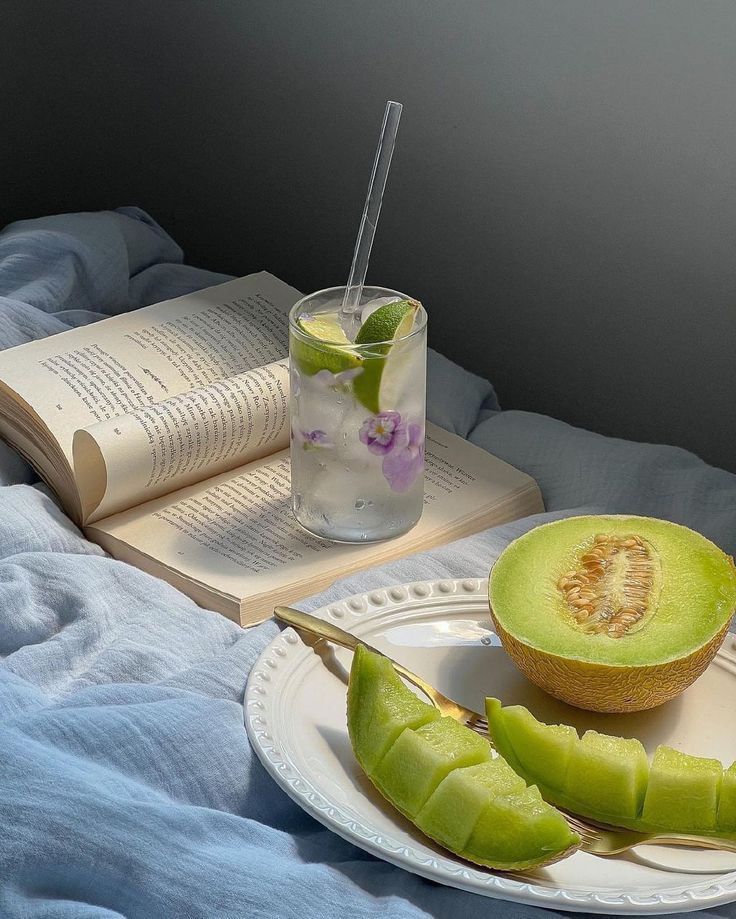 Relaxing moment with a book, refreshing lemon-lime drink, and fresh melon slices on a cozy bed. Perfect for a peaceful retreat.