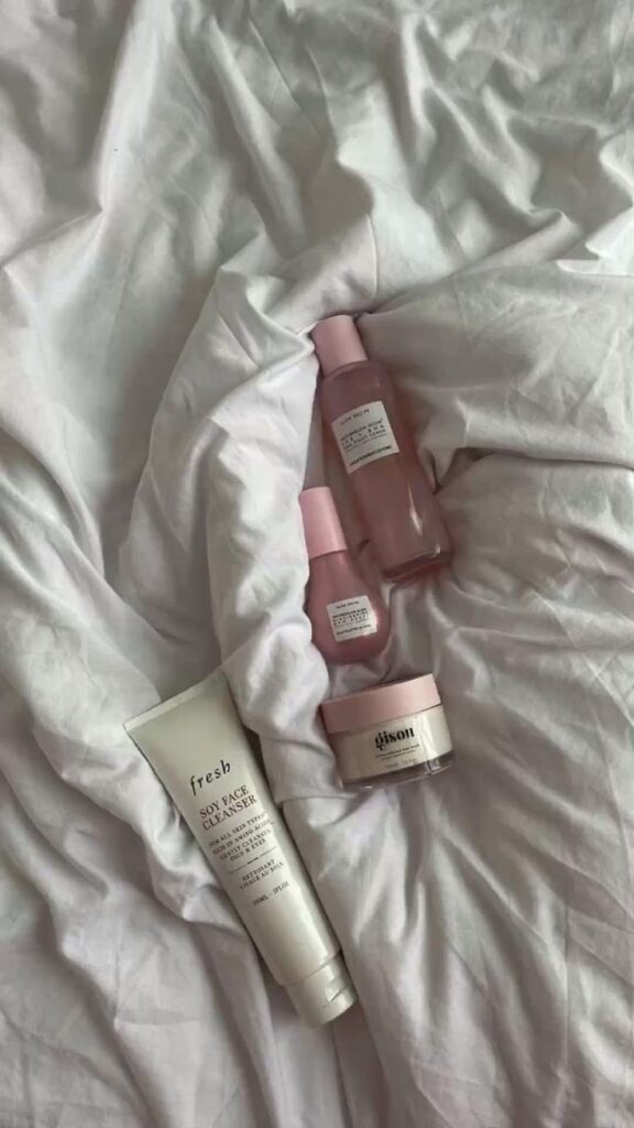 Skincare products arranged on soft white sheets, featuring minimalist packaging in pink and white tones.