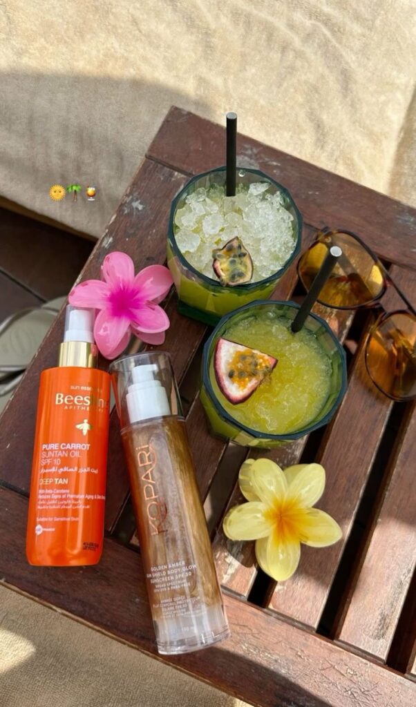 Tropical drinks on a wooden table with sunscreen and vibrant flowers, perfect for a sunny beach day vibe.