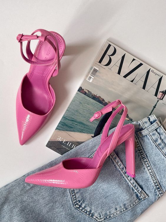 Bright pink high heels on denim jeans, next to a fashion magazine for a chic and trendy look.