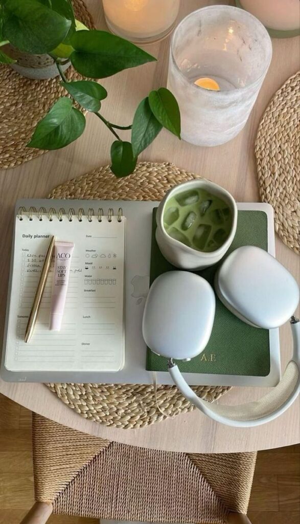 Cozy workspace with daily planner, pen, lip balm, headphones, iced matcha, and green notebook on a woven placemat.