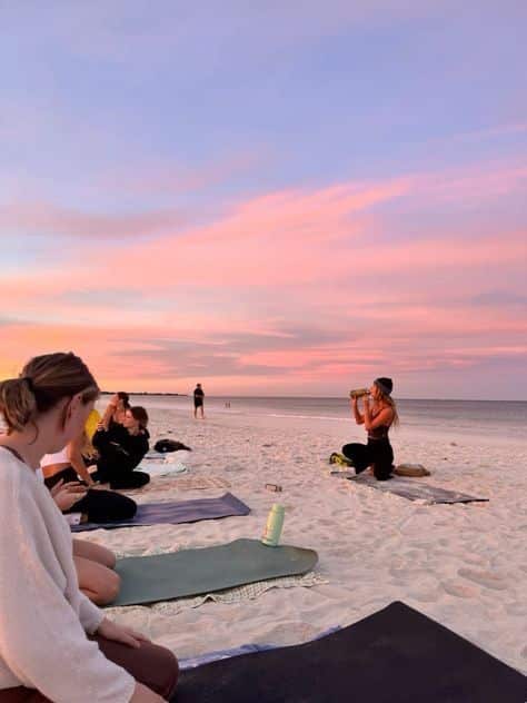 Beach yoga class at sunset with participants on mats enjoying a serene sky. Perfect setting for relaxation and mindfulness.