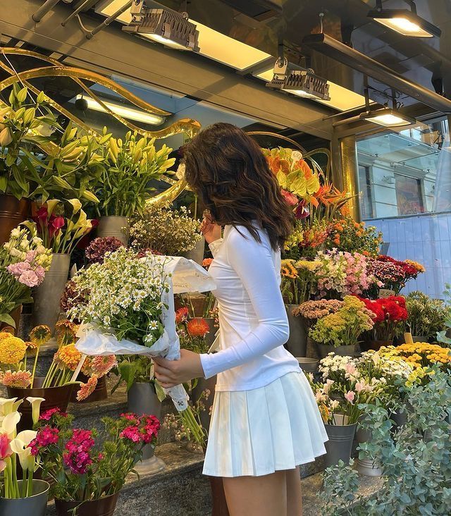 Woman in white dress holding flowers at a vibrant outdoor flower market display.