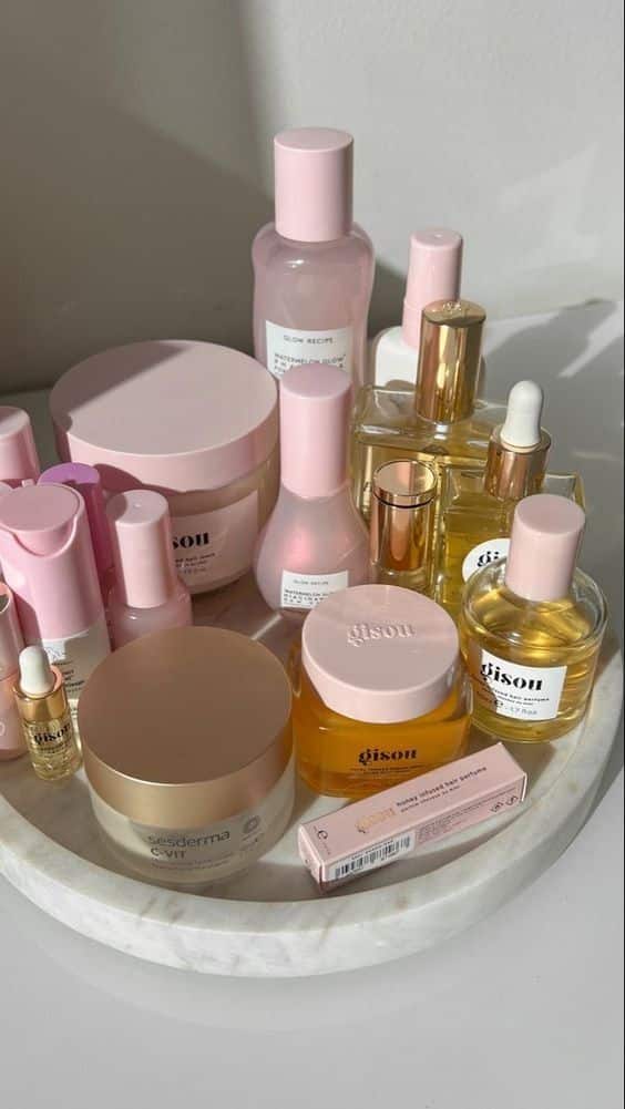A beautiful display of luxury skincare products with pink and gold packaging on a marble tray, illuminated by soft natural light.