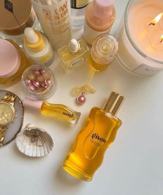 Assorted skincare and beauty products, including oils and serums, arranged stylishly with accessories and a lit candle.