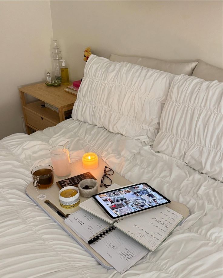 Cozy bed setup with tablet, candles, tea, and planner on a tray, perfect for relaxation or study.