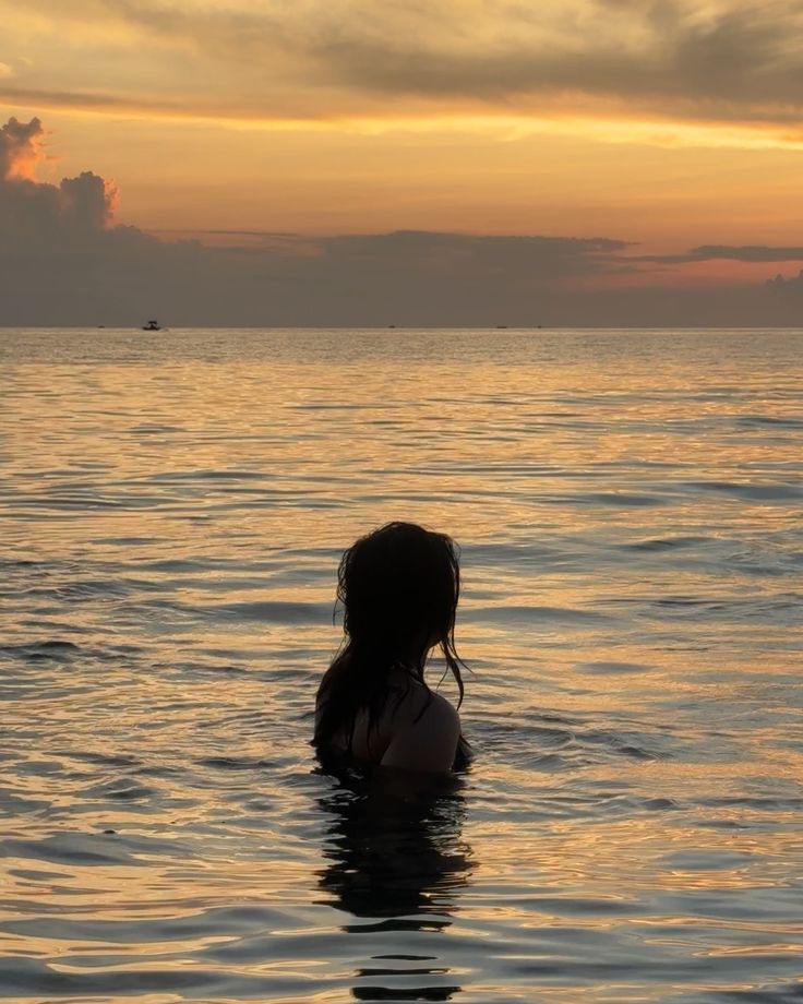 Woman in water at sunset, serene ocean scene, vibrant sky reflecting on waves, peaceful evening swim.